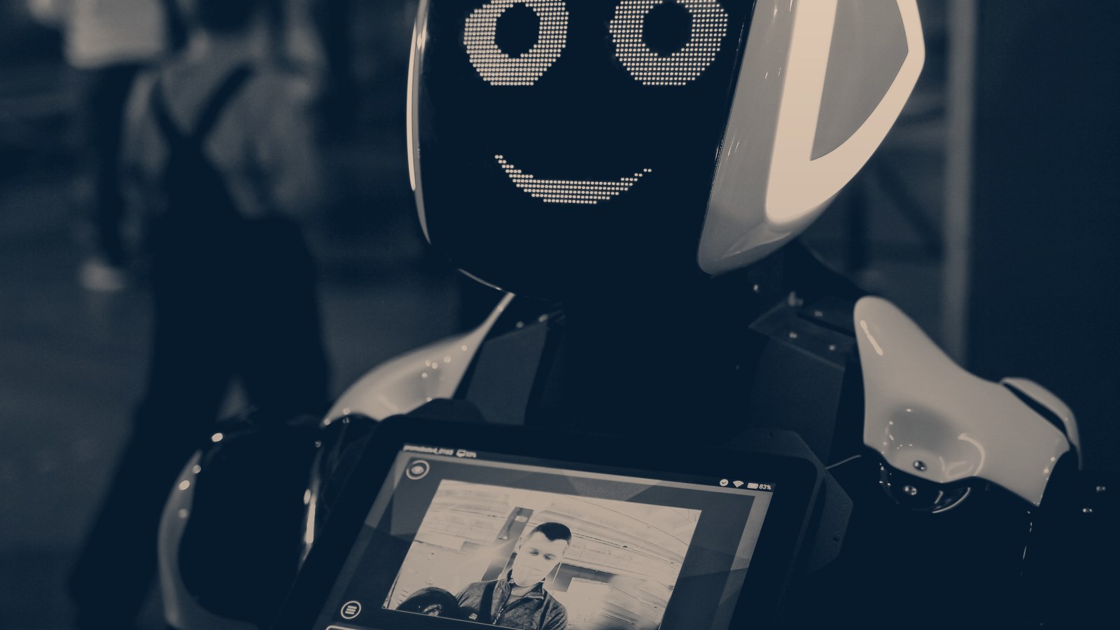 A modern service robot with a smiling LED face and a chest screen showing a person's face, navy duotone.