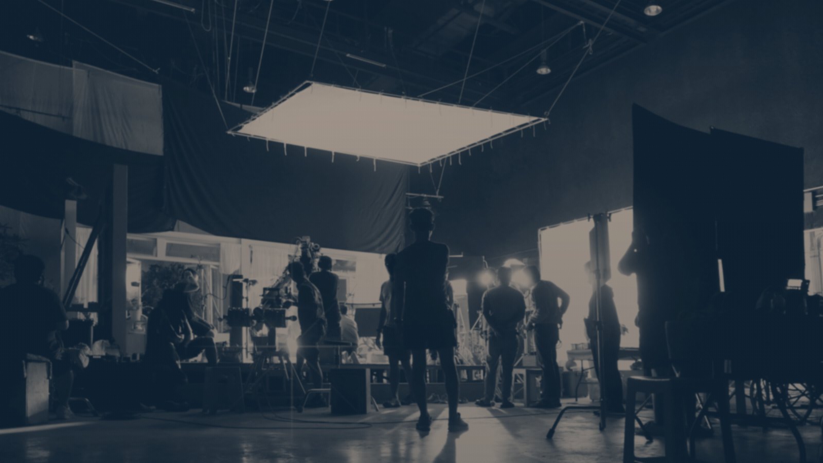 A film crew silhouetted on a big production stage, lit by a single overhead soft box