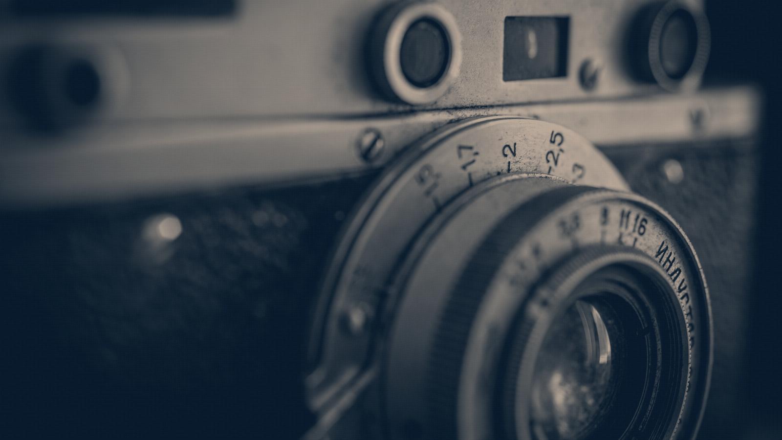 Close up of a battered vintage rangefinder camera, dials worn, lens scratched, navy duotone.