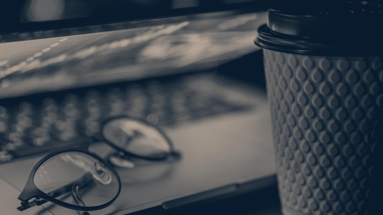 A pair of reading glasses resting on a laptop keyboard, the screen soft behind them, navy duotone.