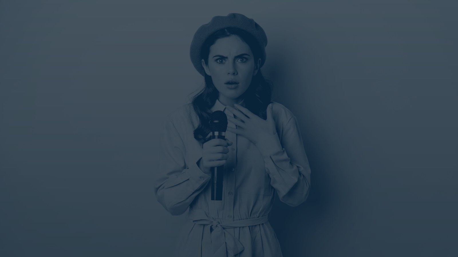 A woman in a beret holding a microphone, caught mid-reaction with a hand to her chest, navy duotone.